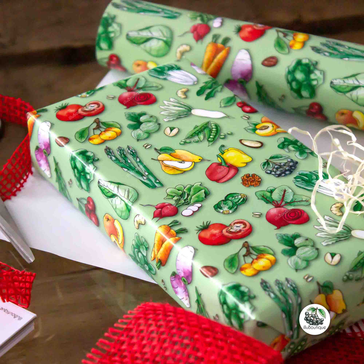 Wunderschönes grünes Geschenkpapier mit bunten handgemalten Obst und Gemüse Illustrationen auf einem Holztisch. Daneben liegt weitere Material um ein Geschenk einzupacken. Eine Schere, ein Kalender, Geschenkband