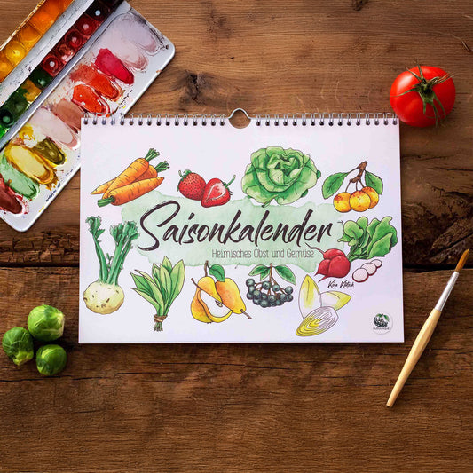 Wandkalender im Querformat mit handgemalten Aquarell-Illustrationen von saisonalem Obst und Gemüse. Der Schriftzug „Saisonkalender“ steht im Mittelpunkt. Daneben liegen frische Tomaten, Rosenkohl, ein Pinsel und ein Farbkasten auf einem Holztisch. Ideal für die Küche oder als Geschenk. Praktisch und dekorativ zugleich. Gedruckt auf hochwertigem Papier. Perfekt für alle, die saisonal und nachhaltig leben möchten.